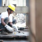Man in safety gear welding metal outdoors, focusing on safety and precision.